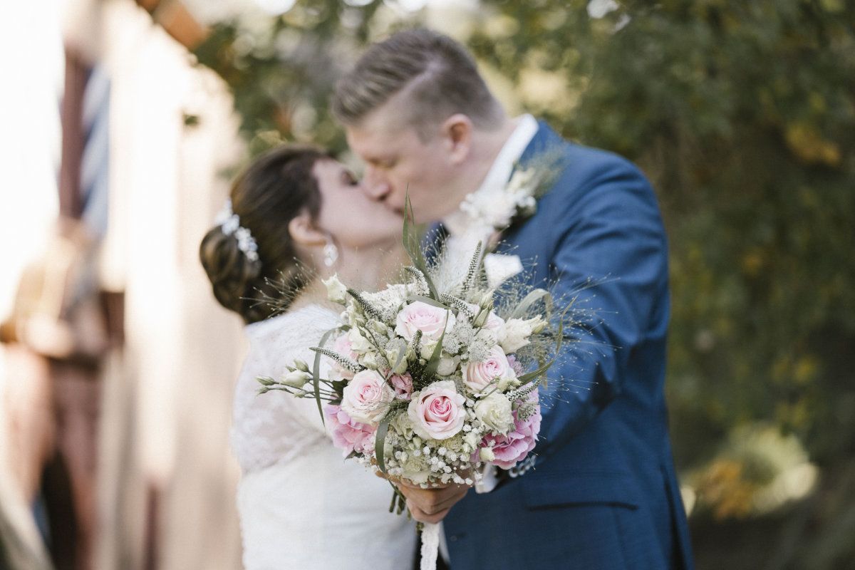 Küssendes Brautpaar mit Brautstrauß im Vordergrund