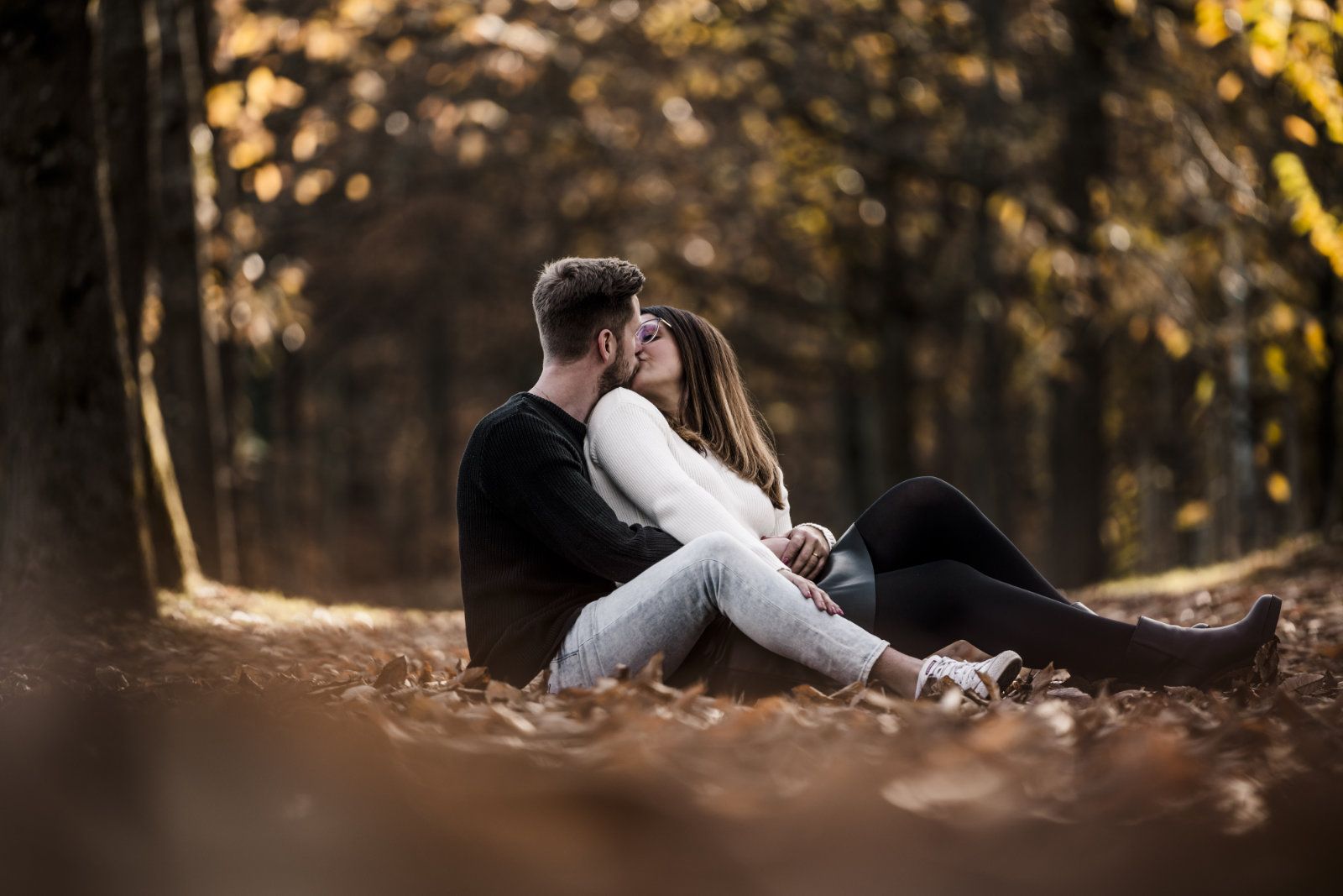 Pärchen küsst sich auf Laub sitzend im Wald, bei einem Herbstshooting 